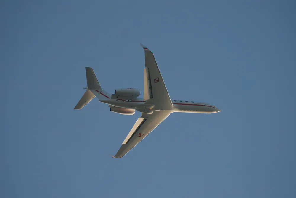 A business jet seen from below, climbing through a clear blue sky